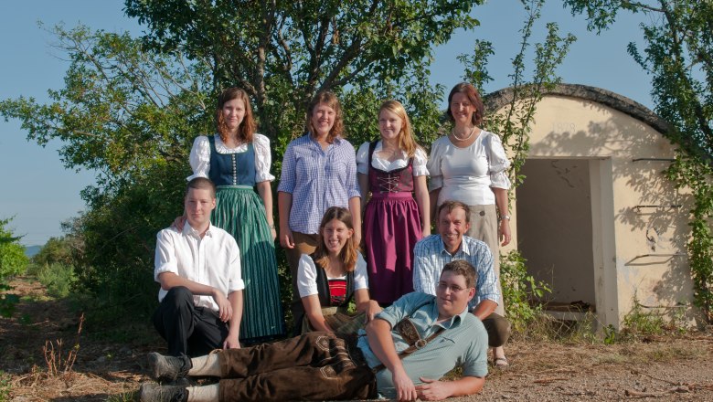 Zöchling family, © Vinterra Zöchling A group of eight people pose outdoors in front of a small building. Some are wearing traditional clothing.