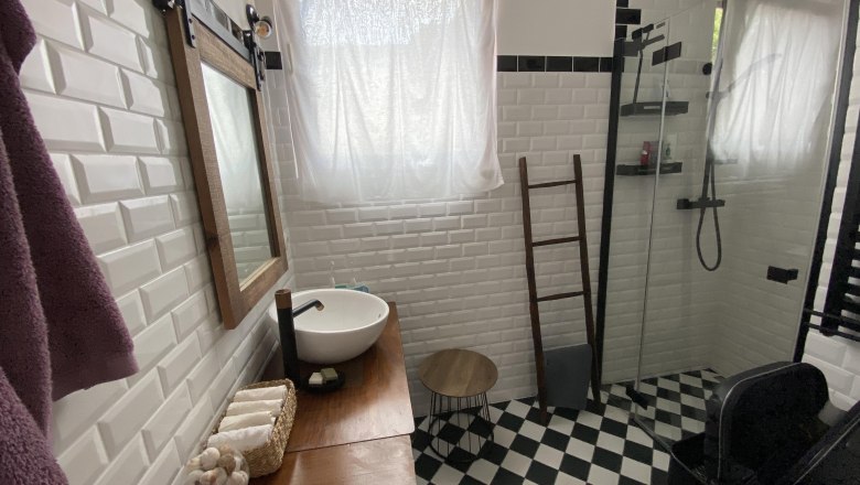 Bathroom, © Katrin Bürger Modern bathroom with white tiled walls, black and white checkerboard floor, washbasin, mirror and shower.