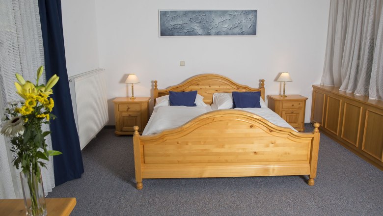 fireworks-in-the-garden, © Besta Betriebs GmbH A bedroom with a wooden double bed, two bedside tables with lamps and a bouquet of flowers on a table.