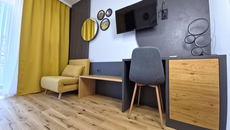 Modern "feel-good room", © Julian Weber, Café Pension Kristall Modern furnished room with yellow armchair, wooden floor, desk and wall decorations.