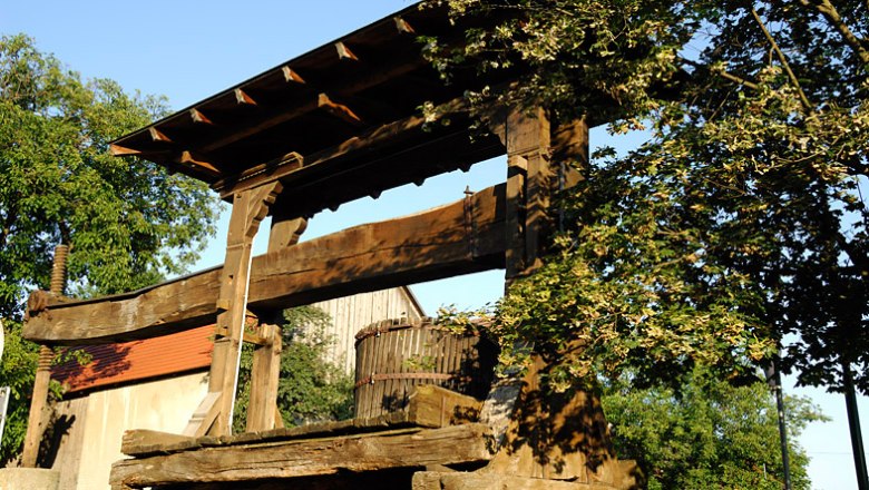 Königsbrunn, © Gemeinde Königsbrunn am Wagram Old wooden wine press outdoors, surrounded by trees and buildings.