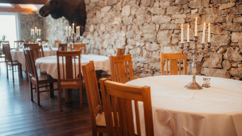 Inn with game cuisine, © Niederösterreich Werbung/Daniela Führer Rustic restaurant with stone wall, wooden furniture and candlesticks.