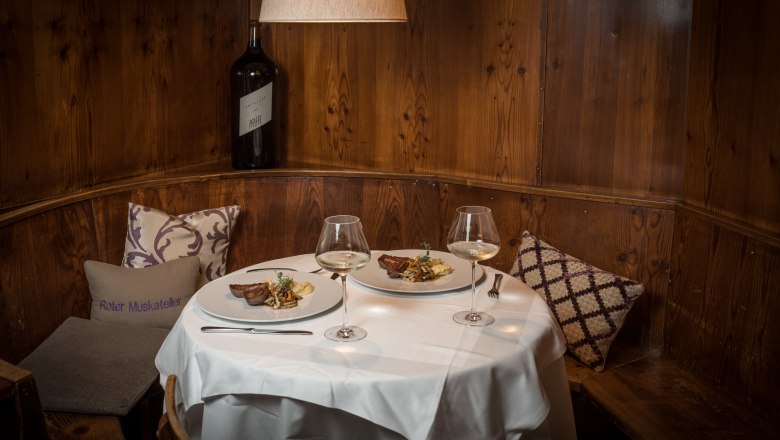 TDR-Hopfeld Dreikönigshof-Gaststube, © Fa. Aumerk Cozy dining room with set table, two plates with food and wine glasses, wooden wall and cushions.