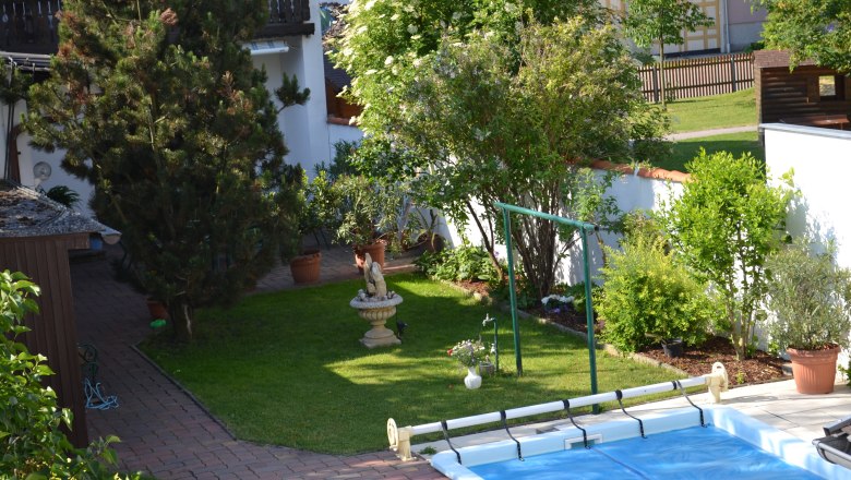 Garden, © Karoline Schmidt A well-tended garden with trees, shrubs, a statue and a pool. A house and a fence can be seen in the background.