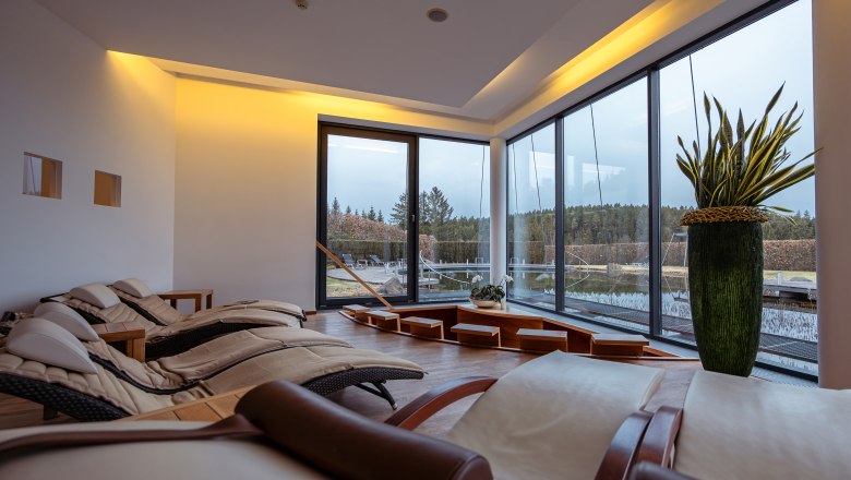 Hotel Schwarz Alm Zwettl, © Niederösterreich Werbung / Maximilian Pawlikowsky Interior view of a modern relaxation room with loungers and large windows with a view of nature.