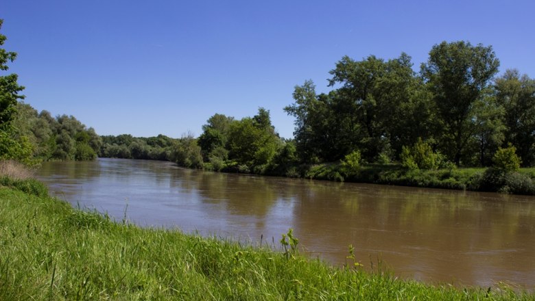 Explore the landscape, © Fam. Lobner River with green banks and trees under a clear blue sky.