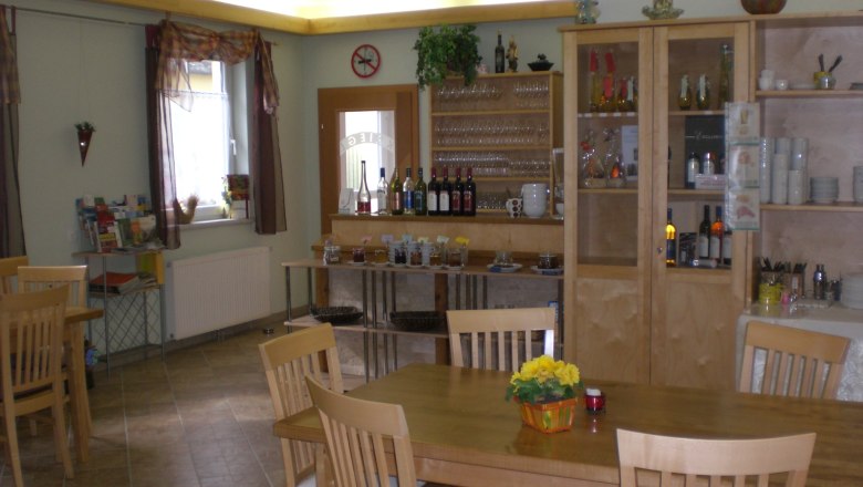 Tasting and breakfast room, © Fam. Kriegl A cozy tasting and breakfast room with wooden furniture, shelves with glasses and bottles, and a table with flowers.