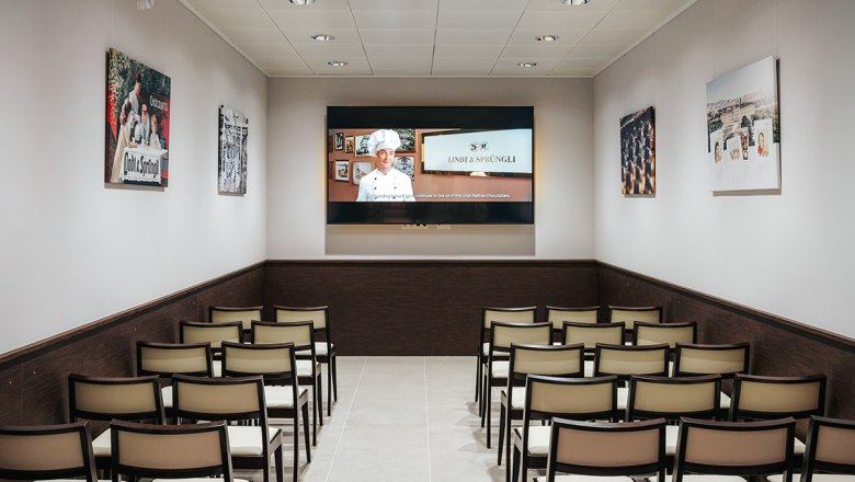 Lecture room, © Philipp Lipiarski An empty lecture room with rows of chairs and a screen showing a presentation by Lindt & Sprüngli.