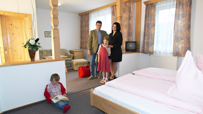 The cozy rooms, © Hausmann/Zwickl Family in a cozy hotel room with wooden furniture and pink bed linen.