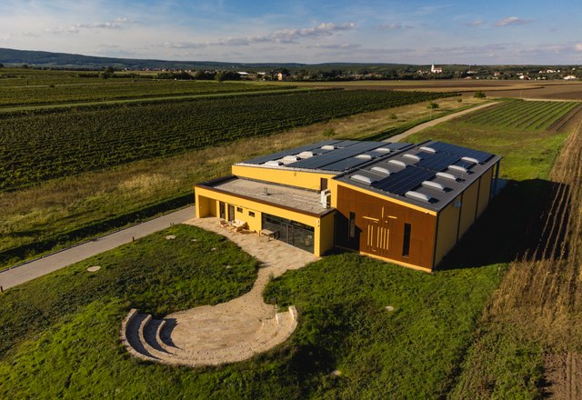The winery from above, © Michael Reidinger Aerial view of a modern winery with solar panels, surrounded by vineyards and fields.