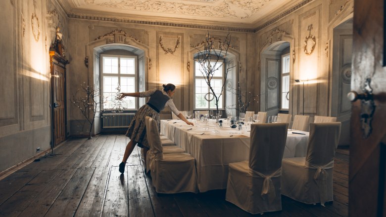 Charming ambience and service, © Hofmeisterei Hirtzberger/Julius Hirtzberger A woman prepares an elegantly laid table in a historic room with ornate walls and ceiling.