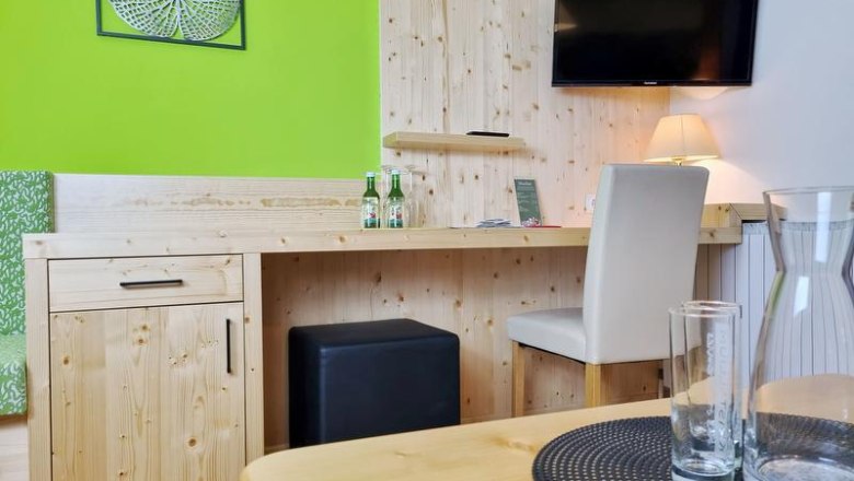 Double room, © Café-Pension Kristall, Julian Weber A hotel room with wooden furniture, a desk, a TV on the wall and green wall decorations.