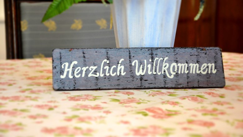 A warm welcome, © Gasthaus und Gästehaus Bsteh A wooden sign with the inscription 'Welcome' stands on a flowery table.