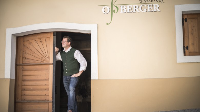 Markus Oßberger in front of his wine tavern, © Nino Zimmerhackl A man stands smiling in the doorway of a building labeled 'Winzerhof Oßberger'.