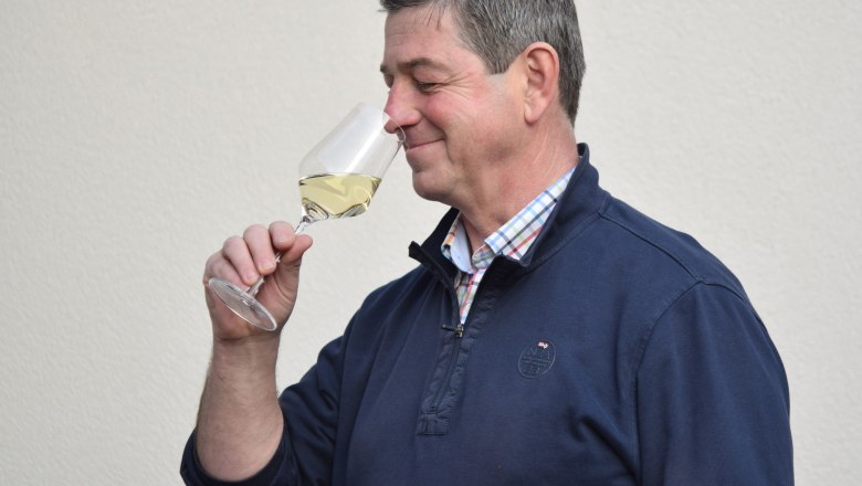 Heurigen host Bernhard Kienberger, © Sophie Kienberger A man smells a glass of white wine against a neutral background.