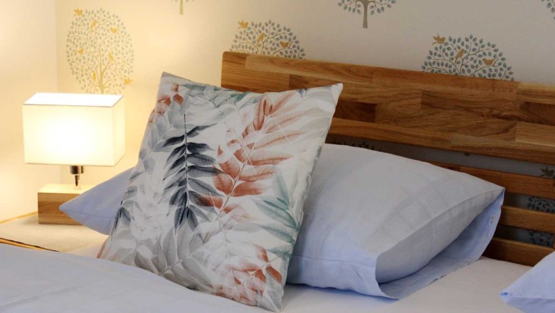 Double room, © Magdalena Donhauser Close-up of a bed with wooden headboard, decorative cushions and bedside lamp.