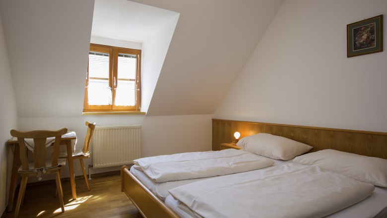 Rooms at the Dinstlhof, © Monika Loeff A simply furnished bedroom with a double bed, a small table and chair under a skylight.
