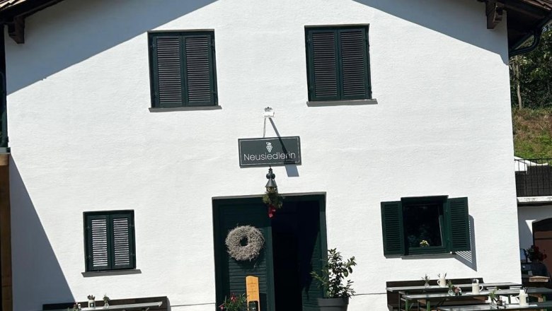 Wine tavern "Die Neusiedlerin", Klein-Neusiedl, © Die Neusiedlerin White building with the inscription 'Neusiedlerin' and wine tables in front of it.