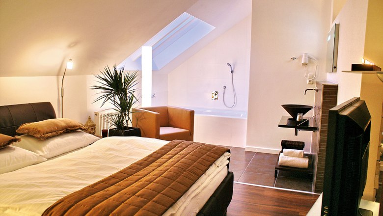 Pension Leichtfried, © Pension Leichtfried Cozy bedroom with double bed, plants, armchair and bathtub under a sloping roof.