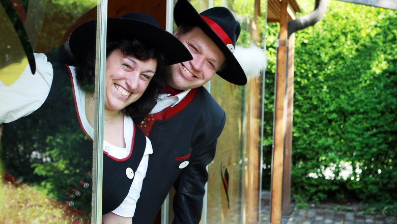 Tavern Moderbacher, © weinfranz.at Two people in traditional costume smile through a window.