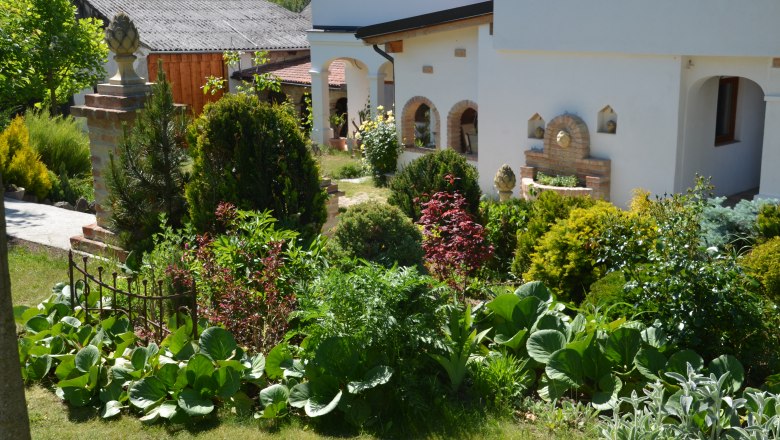 Garden, © Familie Herrmann A well-tended garden with various plants and a white house in the background.