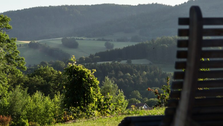View of the garden, © Familie Moser Wooden bench with a view of the hilly landscape and trees in the background.