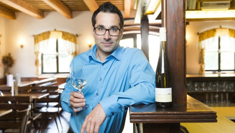 Franz Tanzer at the wine tavern, © Franz Tanzer Man in a blue shirt with a wine glass in a rustic restaurant.