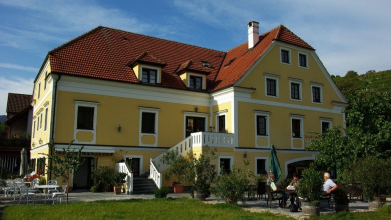 Lagler, © Lagler Yellow building with red roof and terrace, surrounded by trees.