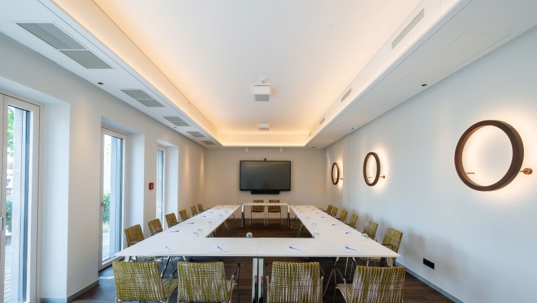 The seminar room, © Philipp Blickfang Modern seminar room with U-shaped table arrangement, chairs, a large screen and decorative wall lamps.