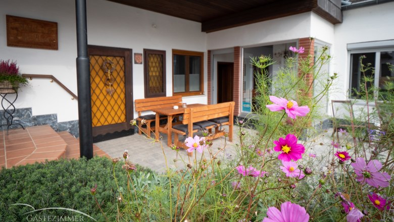 Terrace, © Doris Eminger Terrace with wooden furniture and blooming flowers in the foreground.
