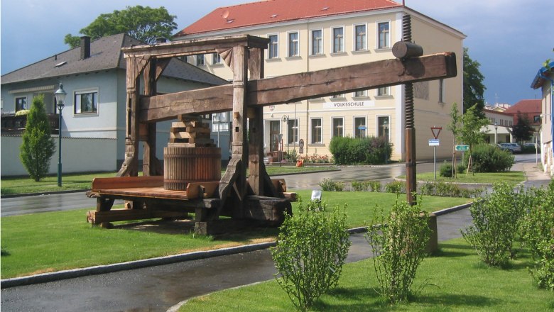 Tree press, © Gemeinde Stetten Historic tree press in front of a school building in a green setting.