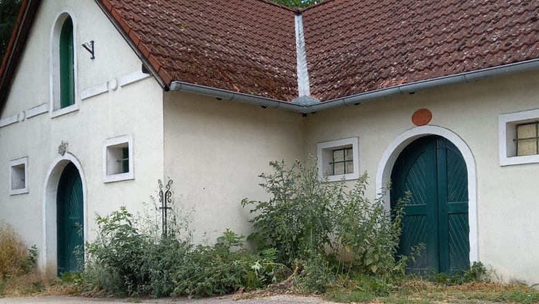 Wine cellar lane Niederleis, © Weinviertel Tourismus Old building with a red tiled roof and green doors, surrounded by plants.