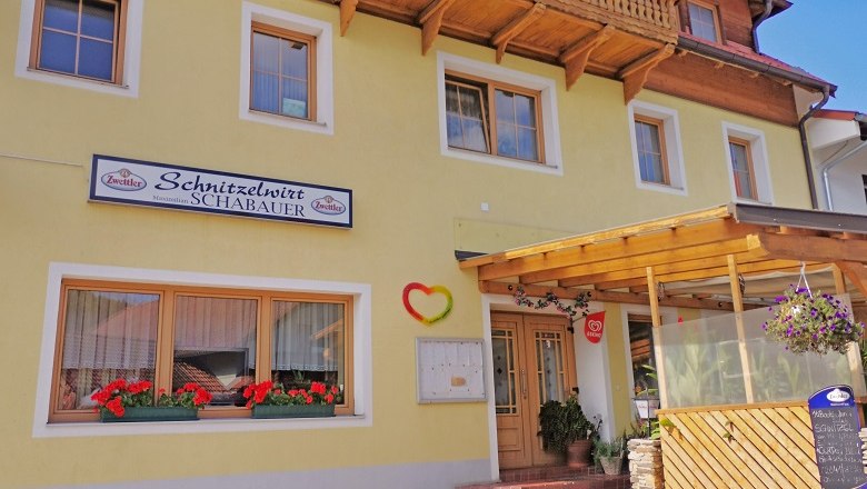 Family business known for its giant schnitzel, © Wiener Alpen Yellow building with sign 'Schnitzelwirt Schabauer', flower boxes and covered entrance.