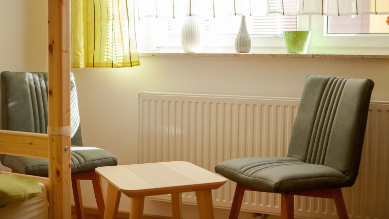 Seating in the bedroom, © Michael Sokolar Two gray chairs and a small wooden table in front of a window with curtains in the bedroom.