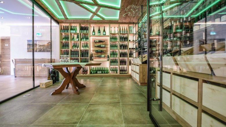 Wine presentation room, © Wachsmann Modern wine presentation room with glass walls, wooden shelves full of wine bottles and a green illuminated ceiling.