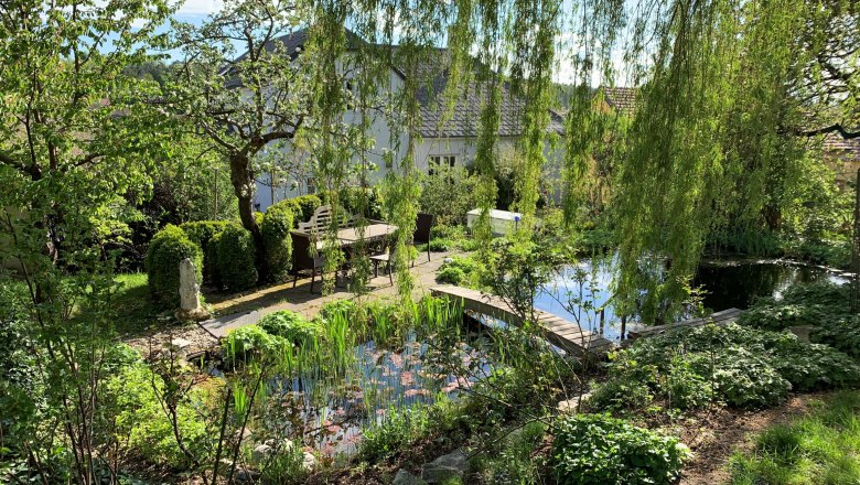Green idyll, © Hofbauer An idyllic garden with a pond, trees and a table and chairs in the open air.