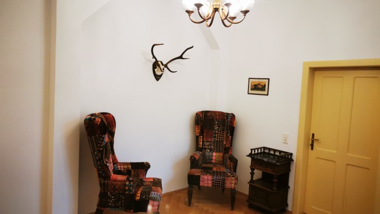 Anteroom in apartment Josef, © Herrnhof Anteroom with two colorful armchairs, antlers on the wall, small table and yellow door.