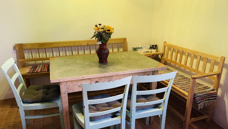 Seating inside, © Fam. Thürr A cozy dining area with a wooden table, two chairs and two benches. There is a vase with sunflowers on the table.