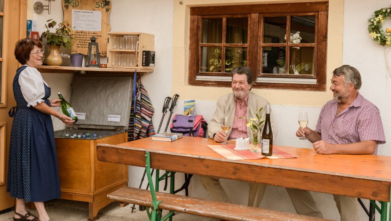Snack in front of the house, © Rita Newman Three people enjoy wine in front of a house, a woman in traditional costume pours.