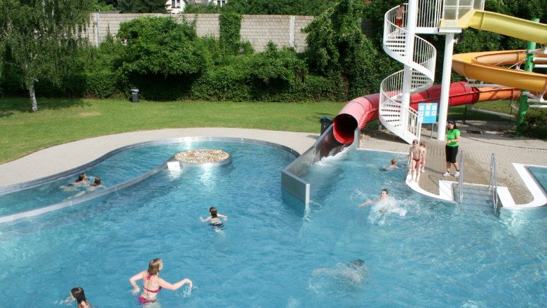 Wienerwaldbad Purkersdorf 1, © WIPUR GmbH An outdoor pool with a water slide and several people in the water.