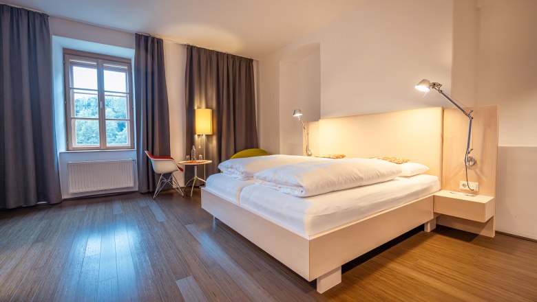 Refugium Hochstrass, © Niederösterreich Werbung / Maximilian Pawlikowsky Modern bedroom with double bed, wooden floor and window with curtains.