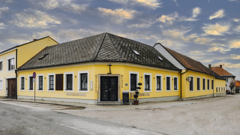 Inn with game specialties, © Niederösterreich Werbung/David Schreiber Yellow inn on a street corner with a cloudy sky in the background.