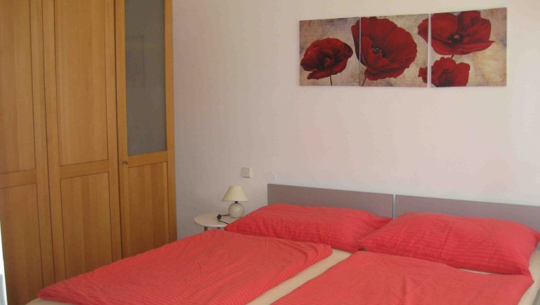 Bedroom, Apartment Gutmann, © Gutmann Double bed with red bed linen and brown wardrobe. There is a picture of red flowers above the bed.