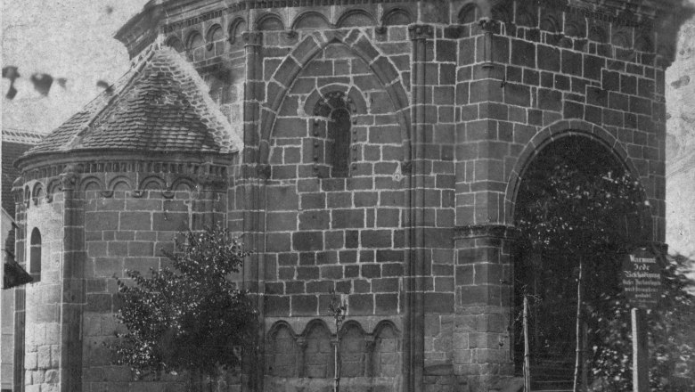 Late Romanesque charnel house, around 1875, © Fotoarchiv Tulln Historical photo of a late Romanesque charnel house with arched windows and tiled roof, surrounded by trees and a path.
