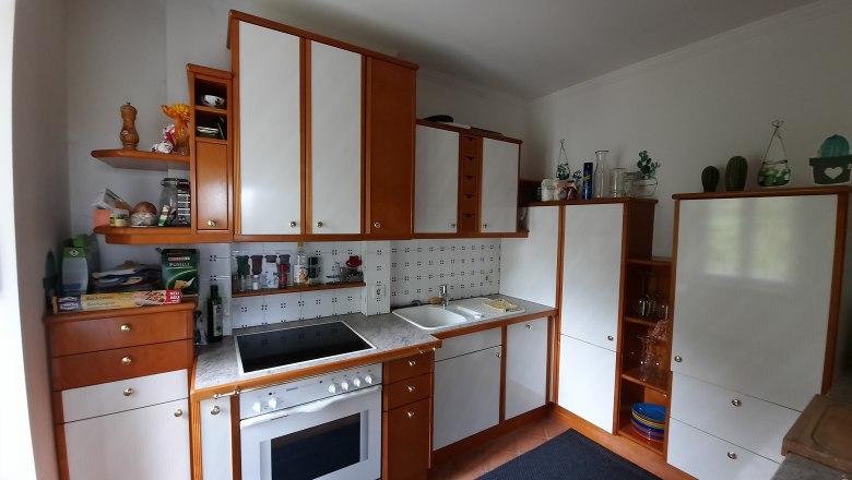 Kitchen, © Dr. Eva Dirnbacher Kitchen with wooden and white cupboards, stove, sink and shelves with spices and decorations.