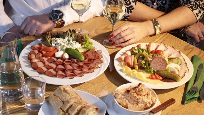 Wine tavern Humer, © Humer Two people sit at a table with platters of cold meats and cheese, bread and wine.