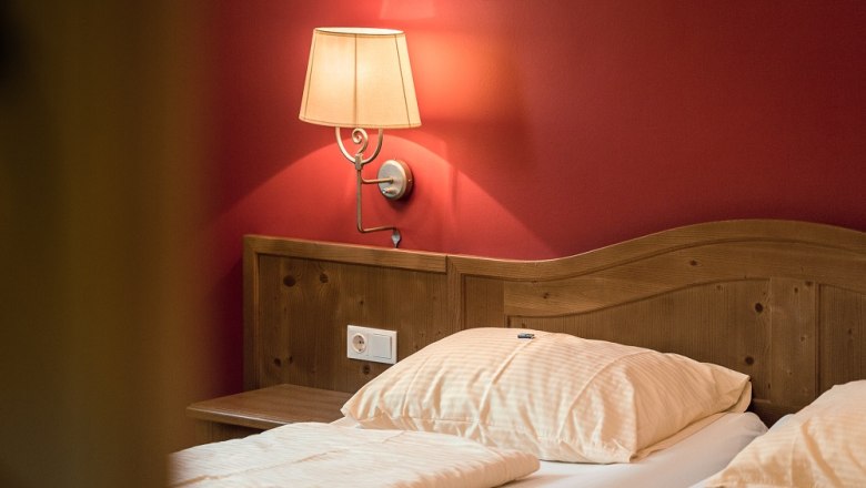 Double room, © Wiener Alpen- Kremsl A cozy double room with wooden headboard, red wall and wall lamp.