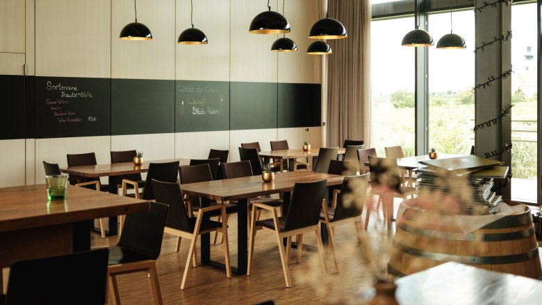 W4, © Weinviertel Tourismus / Michael Reidinger Modern restaurant with wooden tables, black chairs and large windows. Black hanging lamps and a blackboard on the wall.