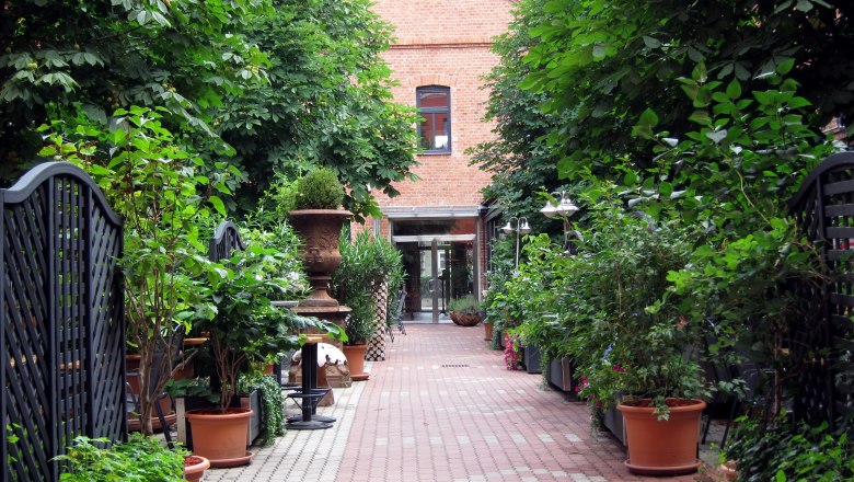 Hotel courtyard, © Hotel Fabrik A paved courtyard with plants in pots and a brick building in the background.