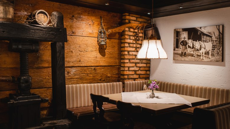 Take a seat in the cozy dining room, © Niederösterreich Werbung/Daniela Führer Cozy dining room with wooden walls, a corner bench, a table with flowers and a lamp. A historical photo hangs on the wall.
